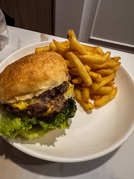 istock A mouth-watering double cheeseburger with melted cheddar cheese and crisp lettuce, perfectly paired with a generous serving of golden, crispy french fries on a white plate. This classic meal is ready 2245962740