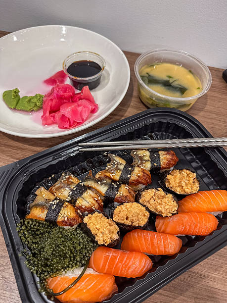A delectable Japanese takeaway feast featuring assorted sushi, fresh salmon nigiri, grilled eel unagi, sea grape gunkan, zesty ginger, wasabi, and savory miso soup, ready for a quick meal.
