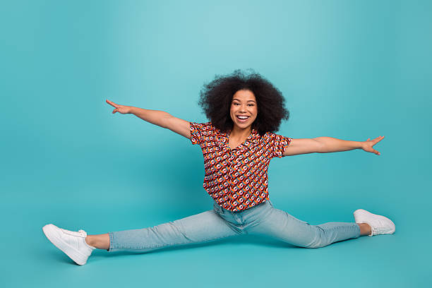 istock Young woman in a colorful printed shirt performs a full side split smiling against a blue background for a dynamic lifestyle fitness and fashion stock photo 2245968606