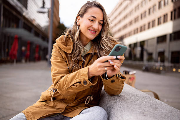 istock Smiling Young Woman Using a Smartphone in Berlin’s Urban Setting While Sitting on a Stone Bench 2245977272