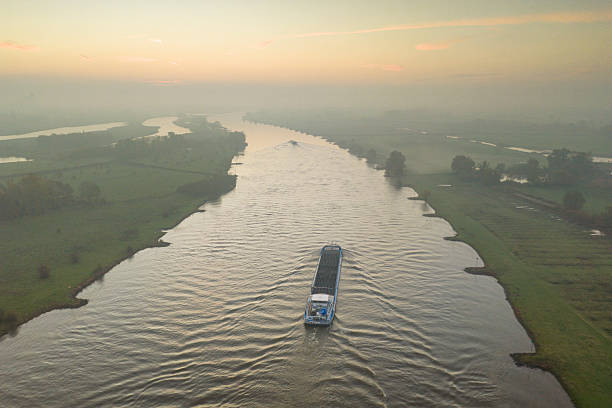 IJssel river meandering through the landscape during a foggy autumn morning near Zwolle and Hattem seen from above. A freight ship barge is sailing into the distance on the river IJssel in Overijssel, Netherlands during an autumn sunrise.