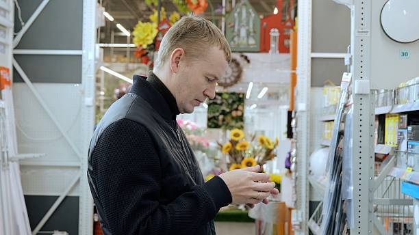 istock Focused blond man comparing products in hardware store aisle for diy renovation. A man in a hardware store choosing a light bulb. translator: good price 2245977686