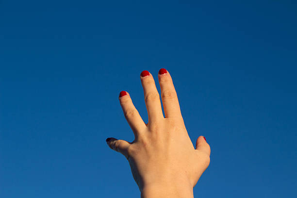A white female hand with red nail polish reaching towards a deep blue sky