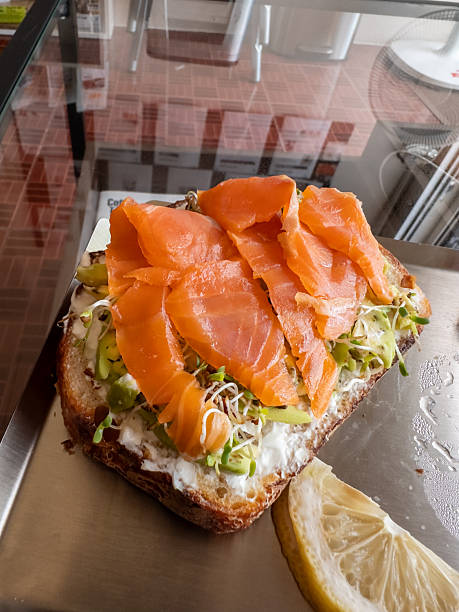 A delicious open-faced toast featuring vibrant smoked salmon, creamy avocado, fresh sprouts, and a spread of cheese, served with a lemon wedge on a sleek metal tray. Perfect for a healthy breakfast or
