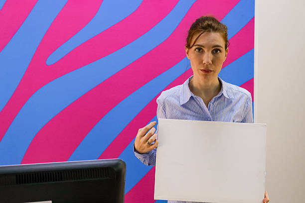 Lady in striped shirt holds white empty panel at counter with monitor and boxes in service point