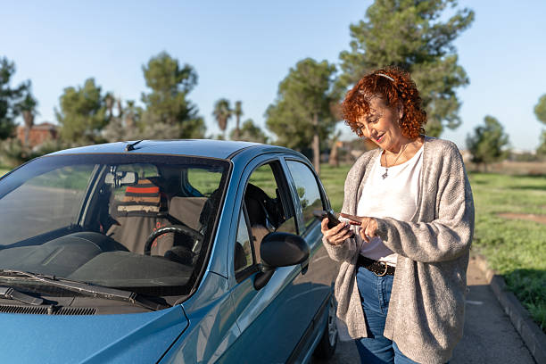 istock Smiling senior woman standing and using mobile phone app next to her car 2245982633