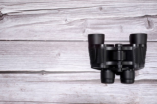 Senior Indian doctor looking through binoculars standing against plain background.