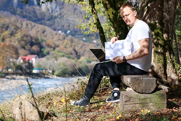 istock Man holding blank paper with laptop on lap in nature 2245983946