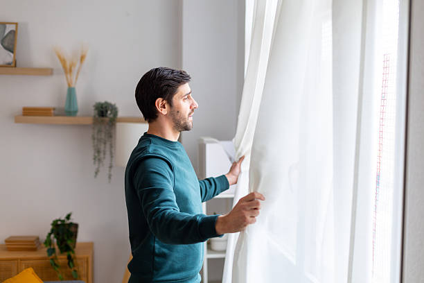istock Man opening curtains looking out window at home 2245986970