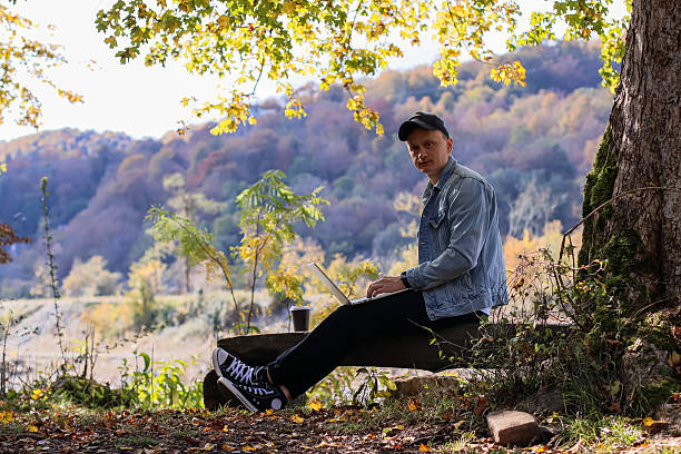 istock Man working on laptop outdoors in autumn forest with mountains 2245989991