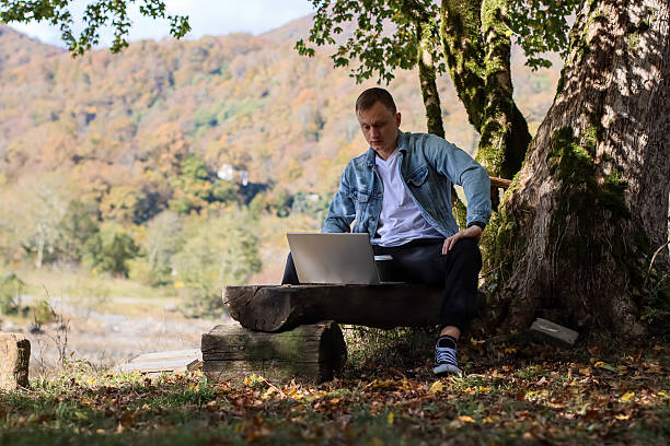 istock Man working on laptop outdoors in autumn forest with mountains 2245990068