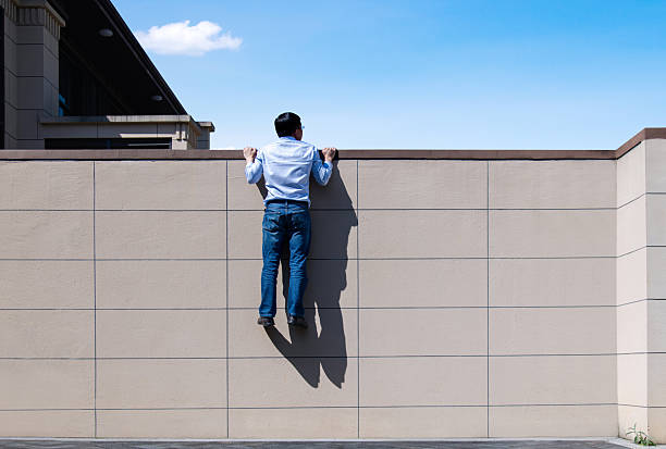 Rotterdam, Netherlands - July 12, 2025: A young Asian man wearing sunglasses and headphones around his neck looks into the camera over a balustrade. In the background is a blue sky with skyscrapers.
