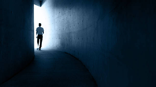 istock Single man walking in narrow and dark corridor to glowing lights 2245990965