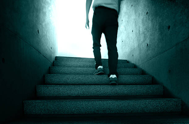 Low section of man climbing stairs toward bright light
