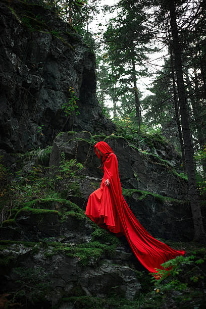 istock woman wearing a long red cloak gracefully walks down a rocky path surrounded by green moss and trees in a dimly lit forest. atmosphere is serene and mysterious 2245991483