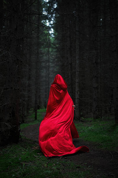 istock figure draped in a striking red cloak navigates a shadowy forest. ethereal scene captures the contrast of vibrant fabric against dark trees, evoking mystery and intrigue 2245991496