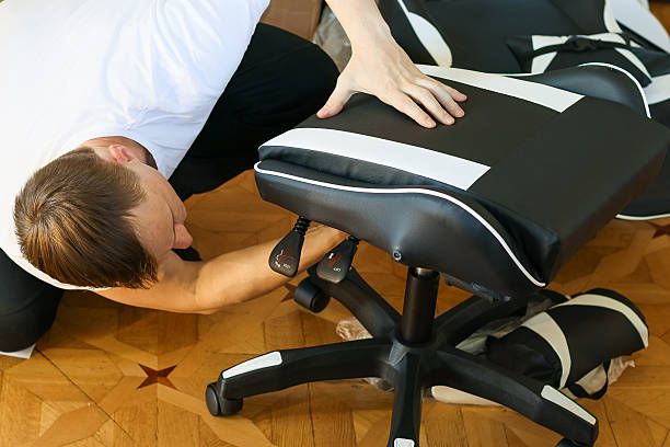 istock Man adjusting levers on upside-down gaming chair seat on floor. 2245992346