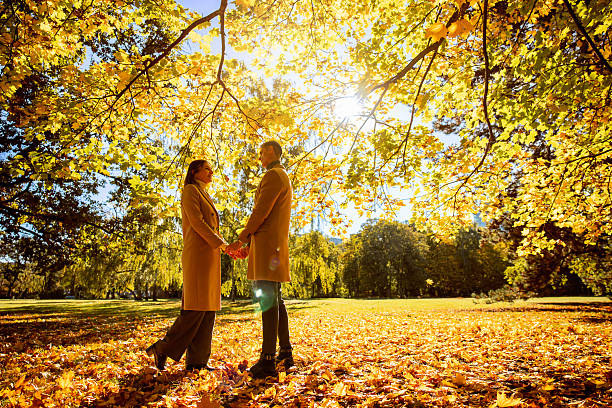 A couple stands hand in hand in a park in Berlin, surrounded by vibrant autumn leaves. The warm sunlight filters through the trees, creating a romantic atmosphere perfect for capturing moments of love and connection.