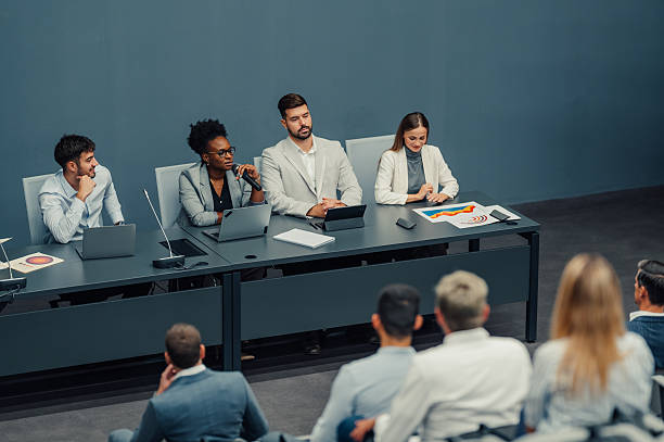 Business people sitting at a table, discussing during a corporate conference, addressing an audience