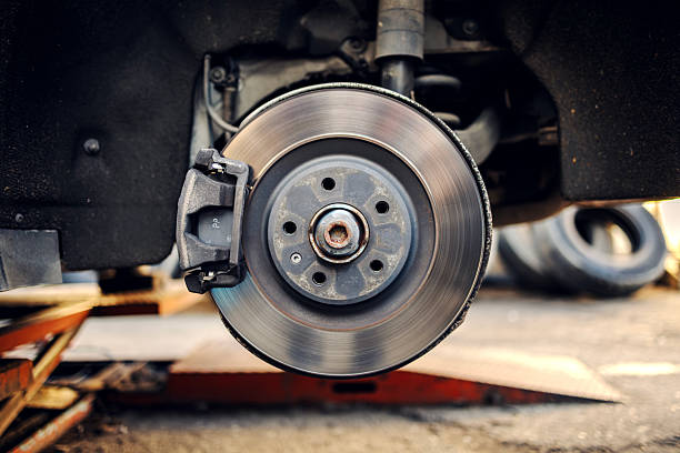 Car brake caliper and disc rotor exposed during maintenance at an auto service workshop, close-up of brake system components and hub