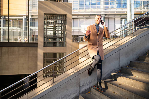 istock Cheerful Businessman Talking on his Smartphone while Standing on Stairs and Leaning Against a Railing 2245995047
