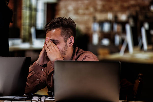 istock Young man sitting with head in hands when struggling with work 2246001495