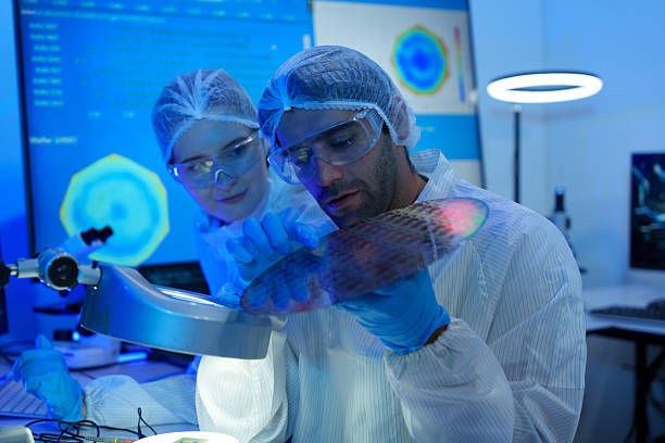 istock International researchers in sterile suits work at a semiconductor manufacturing plant using microscopes. 2246004073