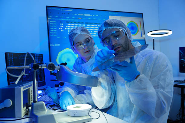 istock International researchers in sterile suits work at a semiconductor manufacturing plant using microscopes. 2246004092