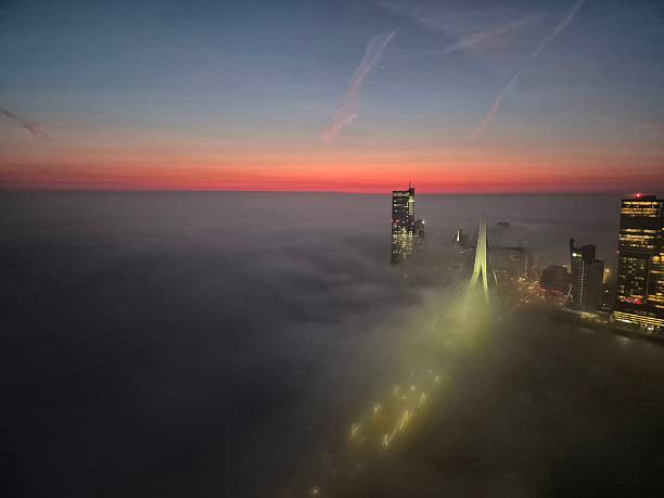 Downtown Rotterdam skyline over river Meuse seen from high angle with fog covering everything except the highest tips of the Erasmus bridge and top of skyscrapers