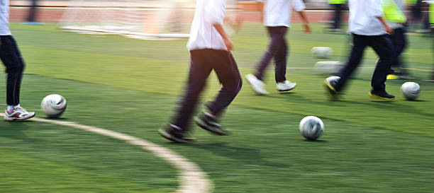 Dynamic image of athlete in green shorts and white shirt, running to strike soccer ball with force, caught mid-motion on field. Concept of professionals sport, competition, tournament, energy, action.