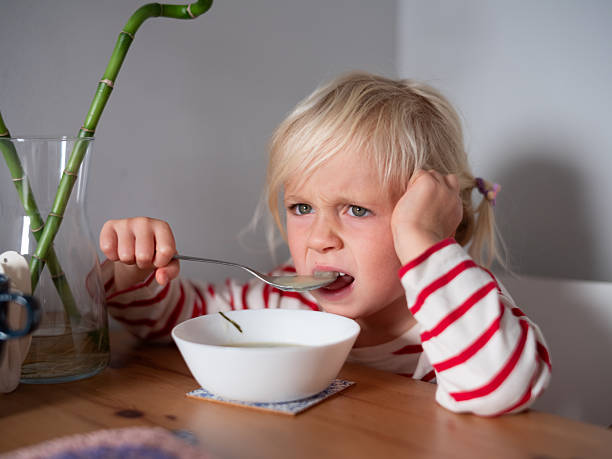istock Four year old blonde child sitting at the table, unhappy while eating soup 2246007444