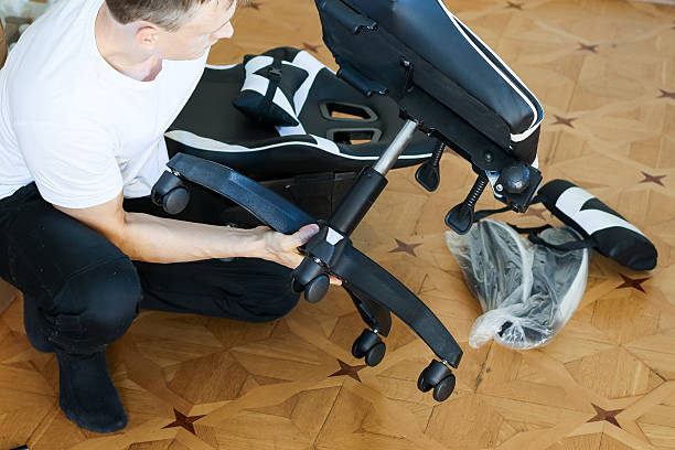 Man fitting wheels to gaming chair base frame on parquet.