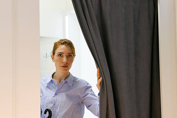 istock Woman peeking through parted gray curtain 2246011812