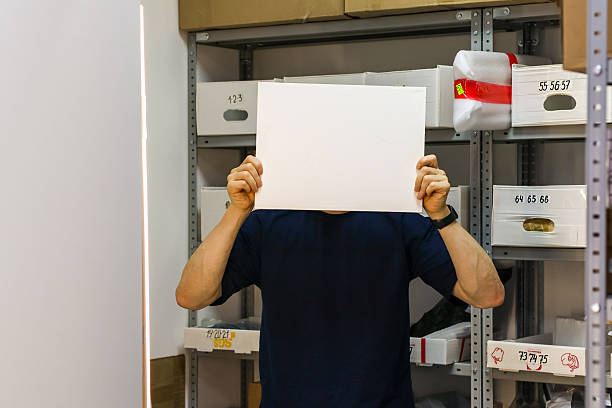 istock Man covering face with held blank paper by shelves 2246012514