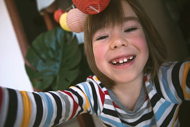 Smiling boy takes a selfie in the warm atmosphere of his children's room. Mobile interaction, self-portrait, everyday play.