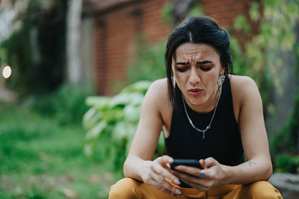 istock Woman sitting outdoors, focused and frustrated while using her smartphone in a garden setting 2246020930