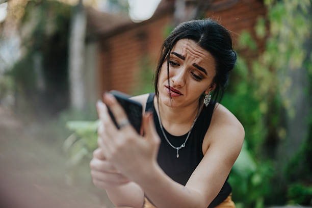 istock Young woman with a worried expression looking at her phone outdoors in a garden setting 2246020965
