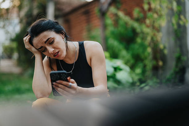Young woman sitting outdoors, looking at her phone with a thoughtful expression