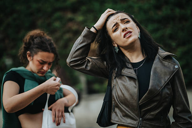 istock Two women outdoors express concern and emotion; one wearing a leather jacket looks distressed while the other checks a bag 2246021052