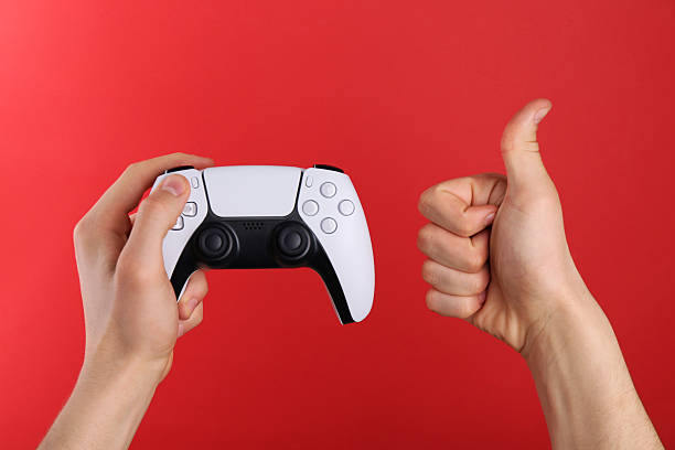 istock Man using wireless game controller and showing thumbs up on red background, closeup 2246023810