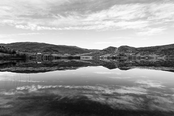 A tranquil black and white landscape featuring a serene lake mirroring rolling hills and a bright sky. Perfect for nature, travel, and zen mood scenes emphasizing symmetry, calm and reflection. Norway