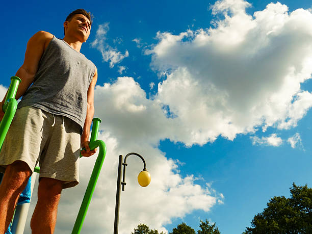 Young handsome man working out in outdoor gym. Sporty guy flexing his muscles on machine. Staying fit and healthy.