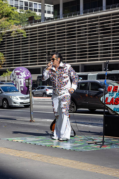 SÃO PAULO, BRAZIL, 7 26 25: An Elvis Presley impersonator delivers a street performance on Avenida Paulista, São Paulo, complete with a dazzling jumpsuit and microphone.