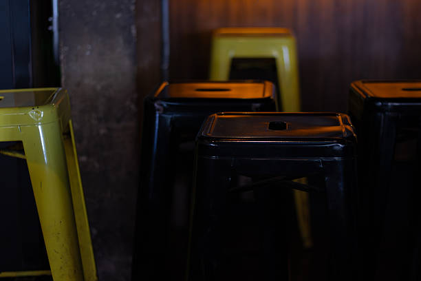 SÃO PAULO, BRAZIL, 7 26 25: A collection of modern yellow and dark metal bar stools in a dimly lit indoor setting.