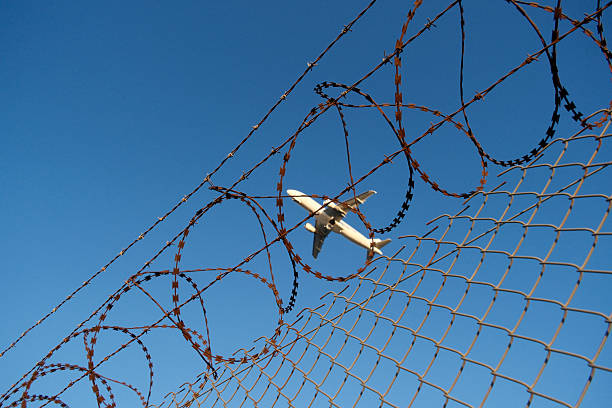 istock Airport barbed wire fence with plane ascending, security concept. 2246032211