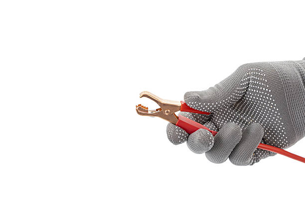 A gloved hand holds opened alligator clip with red cable, isolated on white background. image highlights tool functionality and safety features