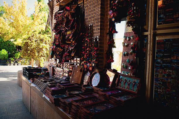 A vibrant market stall displaying various handcrafted items, including colorful textiles, jewelry, and decorative artifacts. The background features lush greenery and warm sunlight filtering through trees.