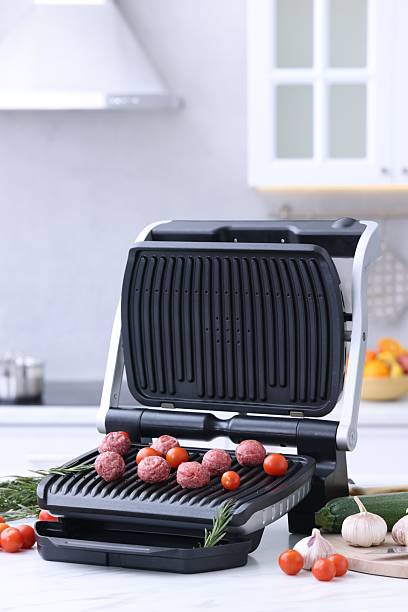 istock Electric grill with meatballs, tomatoes and vegetables on white table in kitchen 2246040003