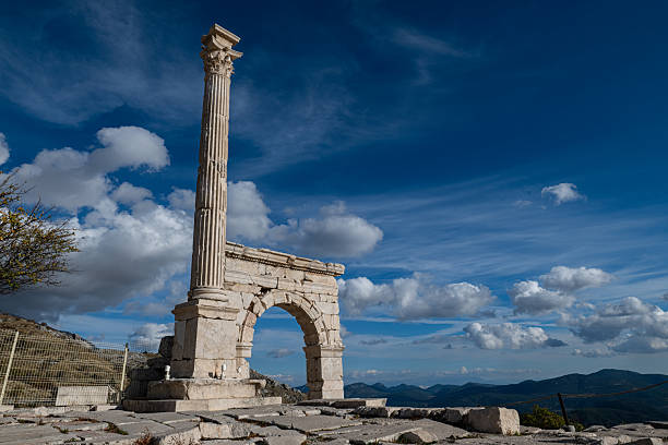 At Sagalassos, an arched monumental gate standing under a blue and cloudy sky, with a column rising above it.