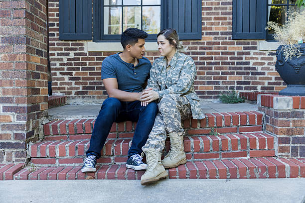 Couple in casual and military attire holding hands on steps. Woman is wearing camouflage uniform, man is in jeans and t-shirt.